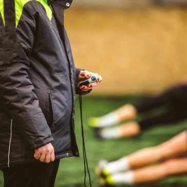 Coach holding stopwatch near athletes exercising.