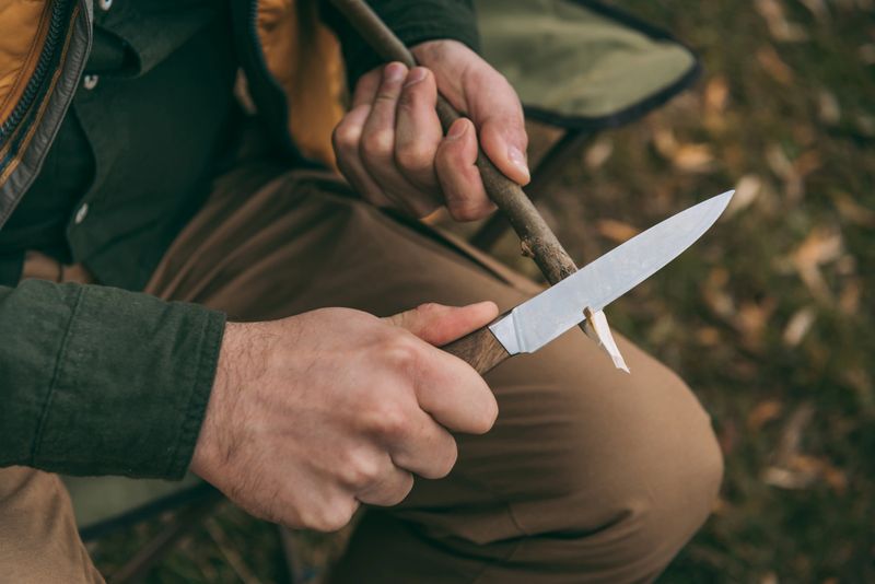 Cropped image of man sharpening a branch for camping