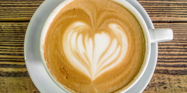 A cup of latte with heart-shaped latte art on a wooden table.
