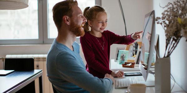 A man and a girl happily using a desktop computer together at home.