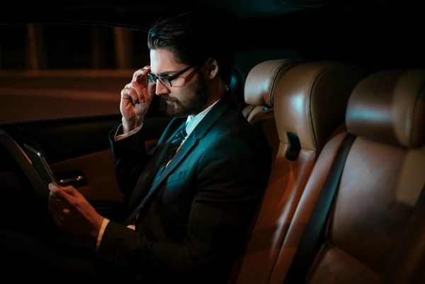 Man in a suit reading a tablet inside a car at night.