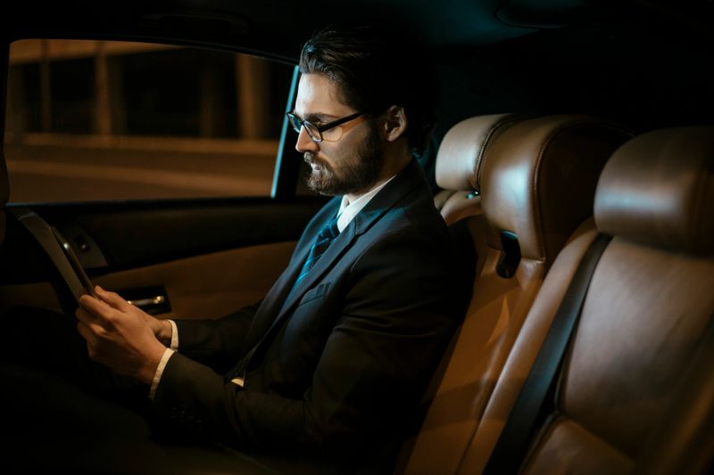 Businessman sitting on back seat and using tablet. Developed from RAW; retouched with special care and attention; Small amount of grain added for best final impression. 16 bit Adobe RGB color profile.
