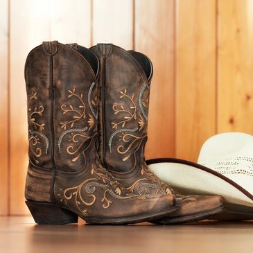Brown cowboy boots and a white cowboy hat placed on a wooden surface.