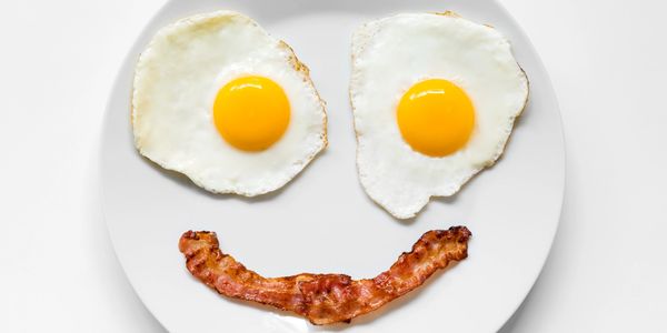 Two sunny-side-up eggs and a bacon strip arranged as a smiley face on a white plate.