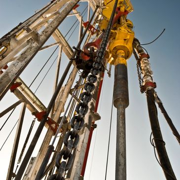 Close-up of oil rig drilling mechanism with chains and pipes against clear sky.