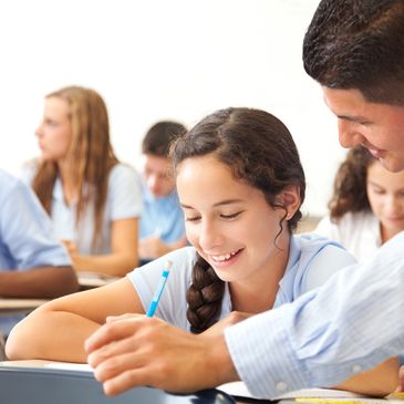 Teacher helping a smiling student with schoolwork in class.