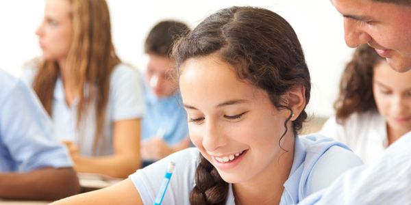 Teacher helping a smiling student with her schoolwork in a classroom.