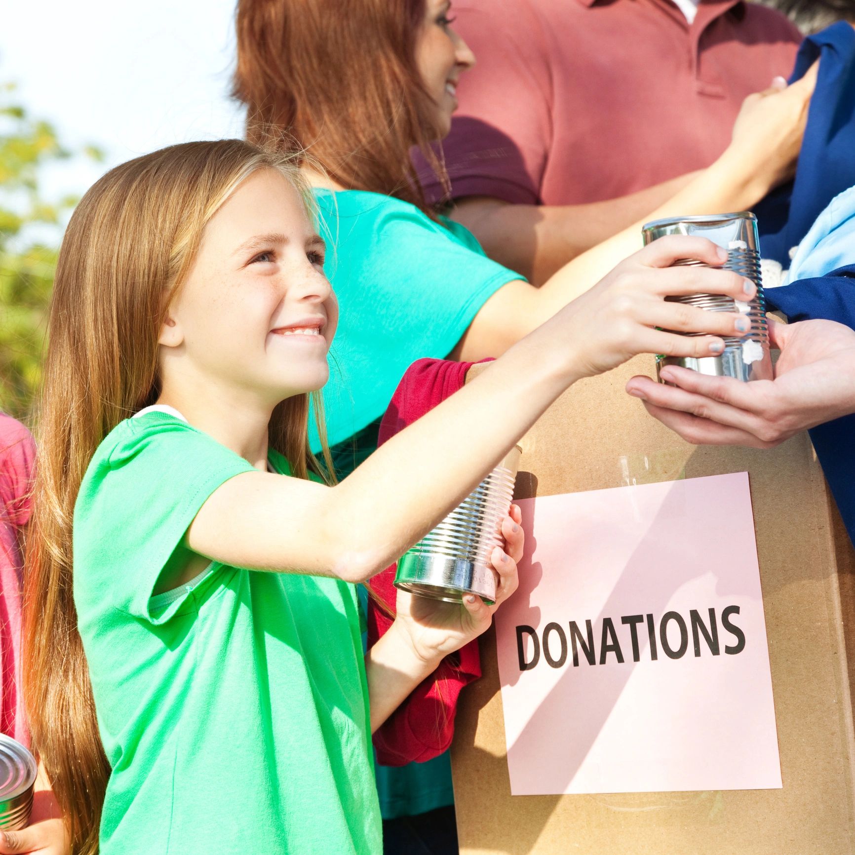A young girl happily donates canned goods to a collection box labeled donations.