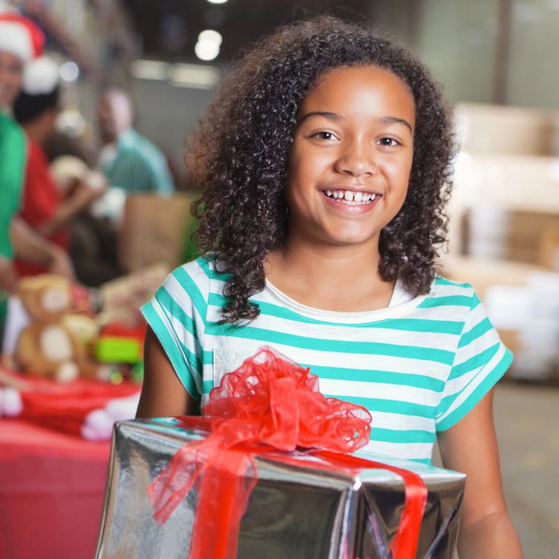 Adorable African American girl holds a wrapped Christmas present during charity event. She is donating the gift to a child in need.