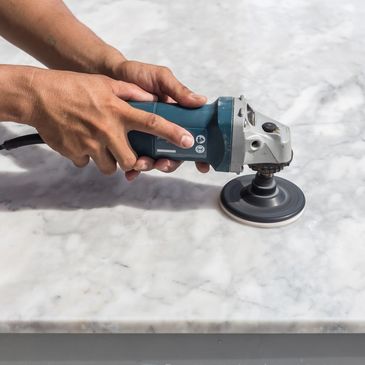 Hands using a power tool to polish a marble surface.