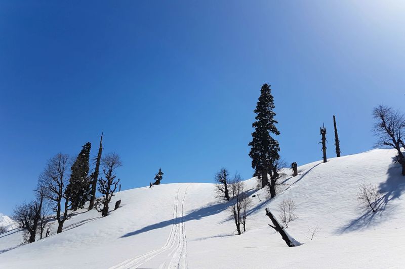 Tracks of snowmobile heading to top of snow mountain in strong sunlight day with blue sky background shoot from mobile camera.