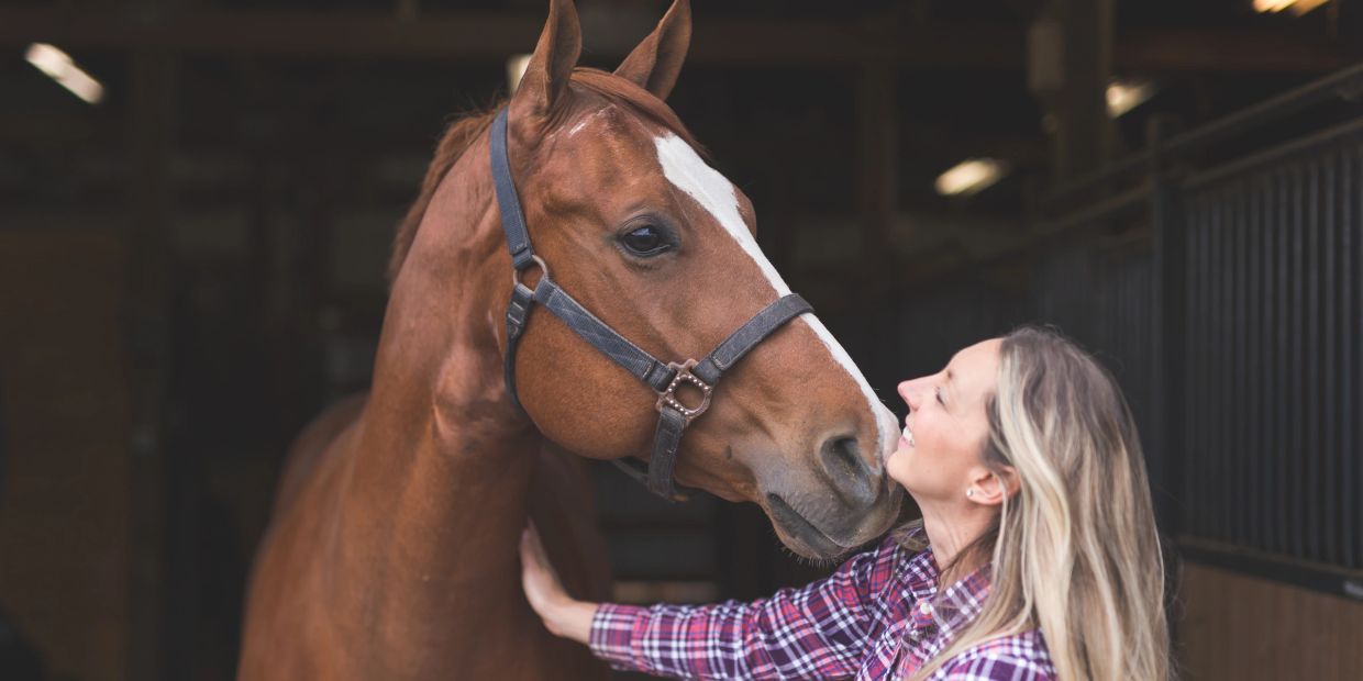 Woman affectionately interacting with a horse in a stable.