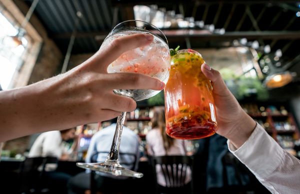 Two people clinking colorful cocktails in a lively bar.