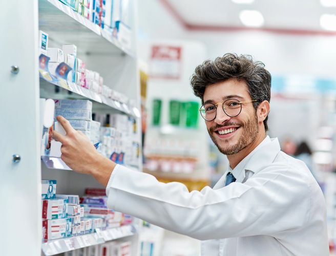 Smiling pharmacist organizing products on a pharmacy shelf.