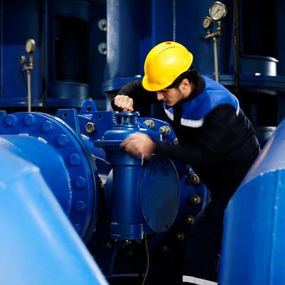 Worker in a yellow helmet operating blue industrial machinery.
