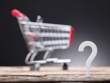 Shopping cart with a question mark on wooden surface.