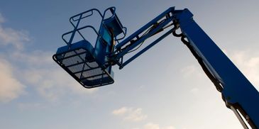 A blue aerial work platform against a partly cloudy sky.