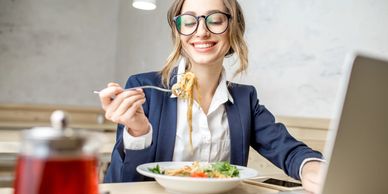 Smiling woman eating noodles at her desk.