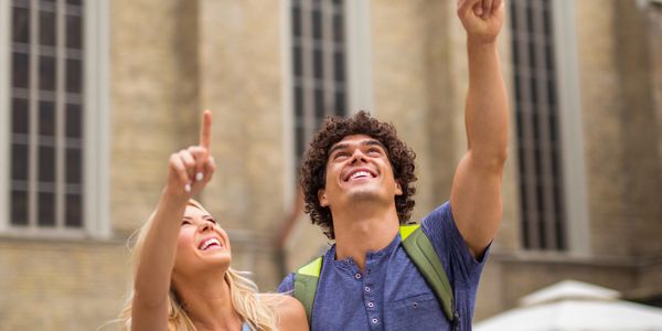 A happy couple pointing upwards and looking excited outdoors.
