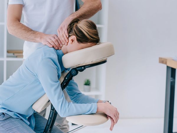 A woman receiving a seated neck massage in a bright office setting, festival, convention, school or office. 