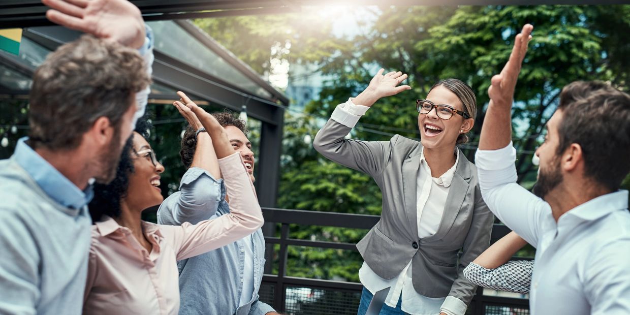 A group of happy colleagues giving high fives during a meeting outdoors.