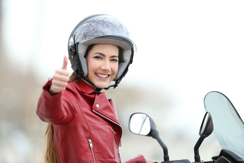 Satisfied motorbiker gesturing thumbs up on her motorcycle outdoors