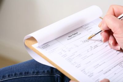 Filling out a new patient registration form on clipboard.
