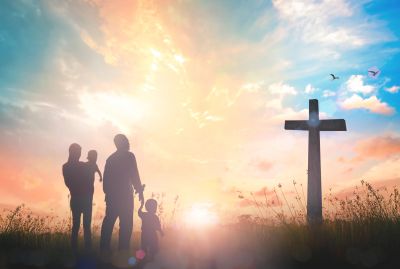 Family silhouette with a cross at sunset.