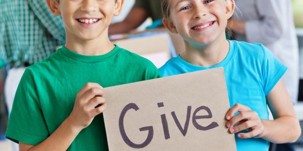 Two smiling kids holding a 'Give' sign.