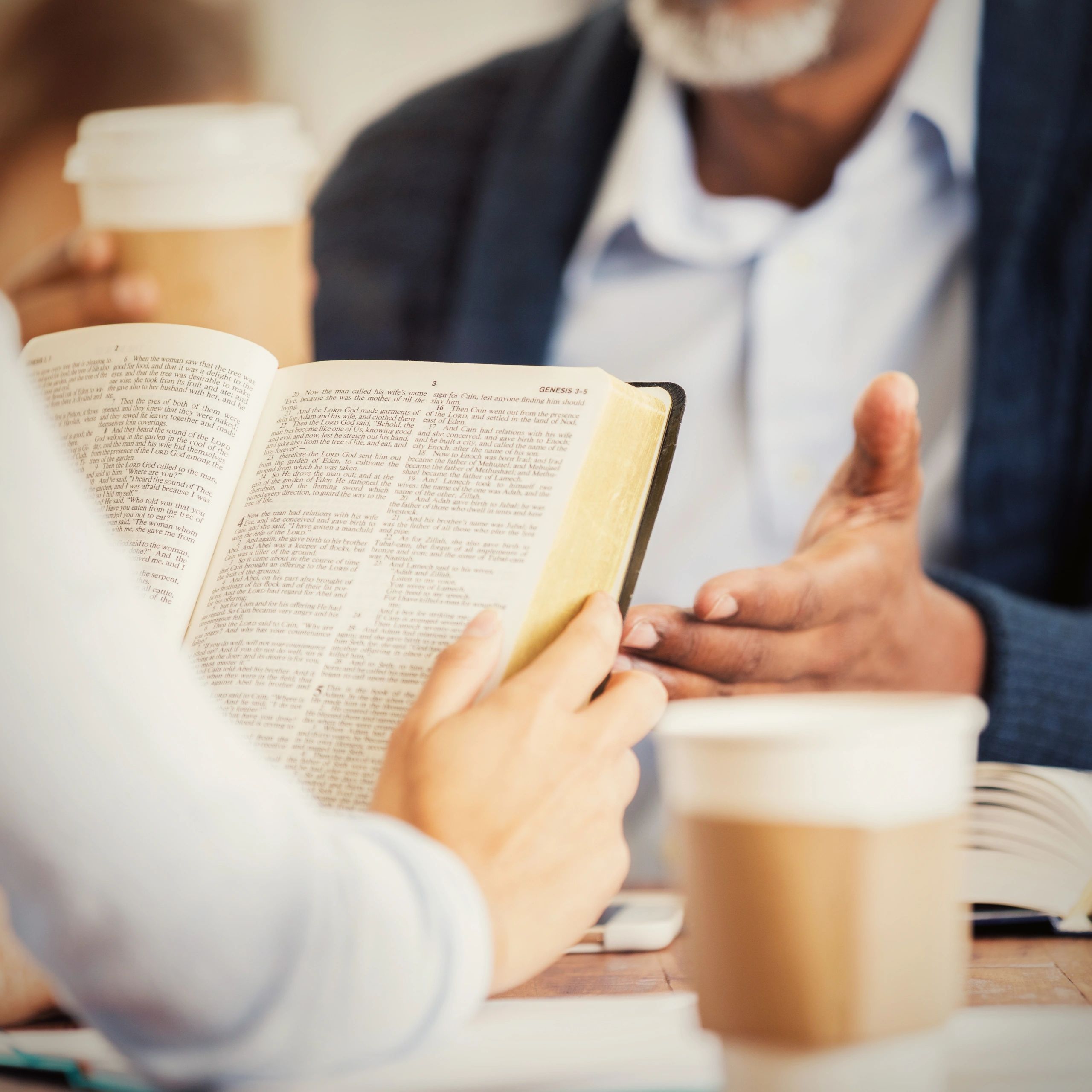 Two people discussing a Bible over coffee.