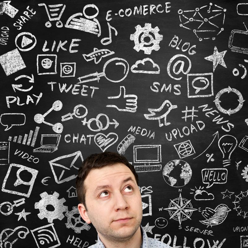 Man looking at social media related icons and words drawn with chalk on blackboard