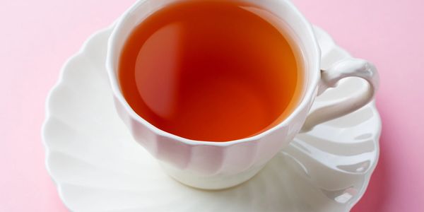 A white teacup filled with tea on a matching saucer against a pink background.