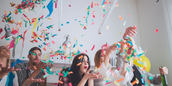 Group of friends joyfully throwing colorful confetti indoors.
