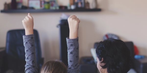 Child raising hands enthusiastically while sitting beside an adult.