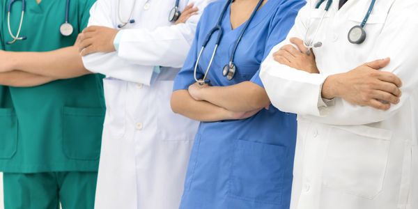 Medical professionals in scrubs and lab coats with stethoscopes, arms crossed.