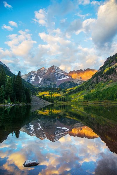 Snow-capped mountains reflecting in a serene lake under a partly cloudy sky.