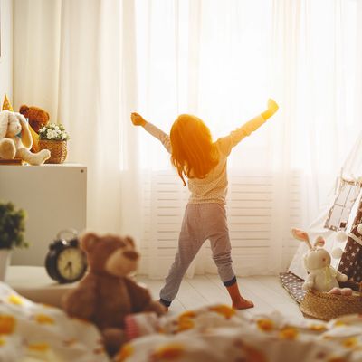 Child stretching in a cozy, sunlit bedroom filled with toys and a play tent.