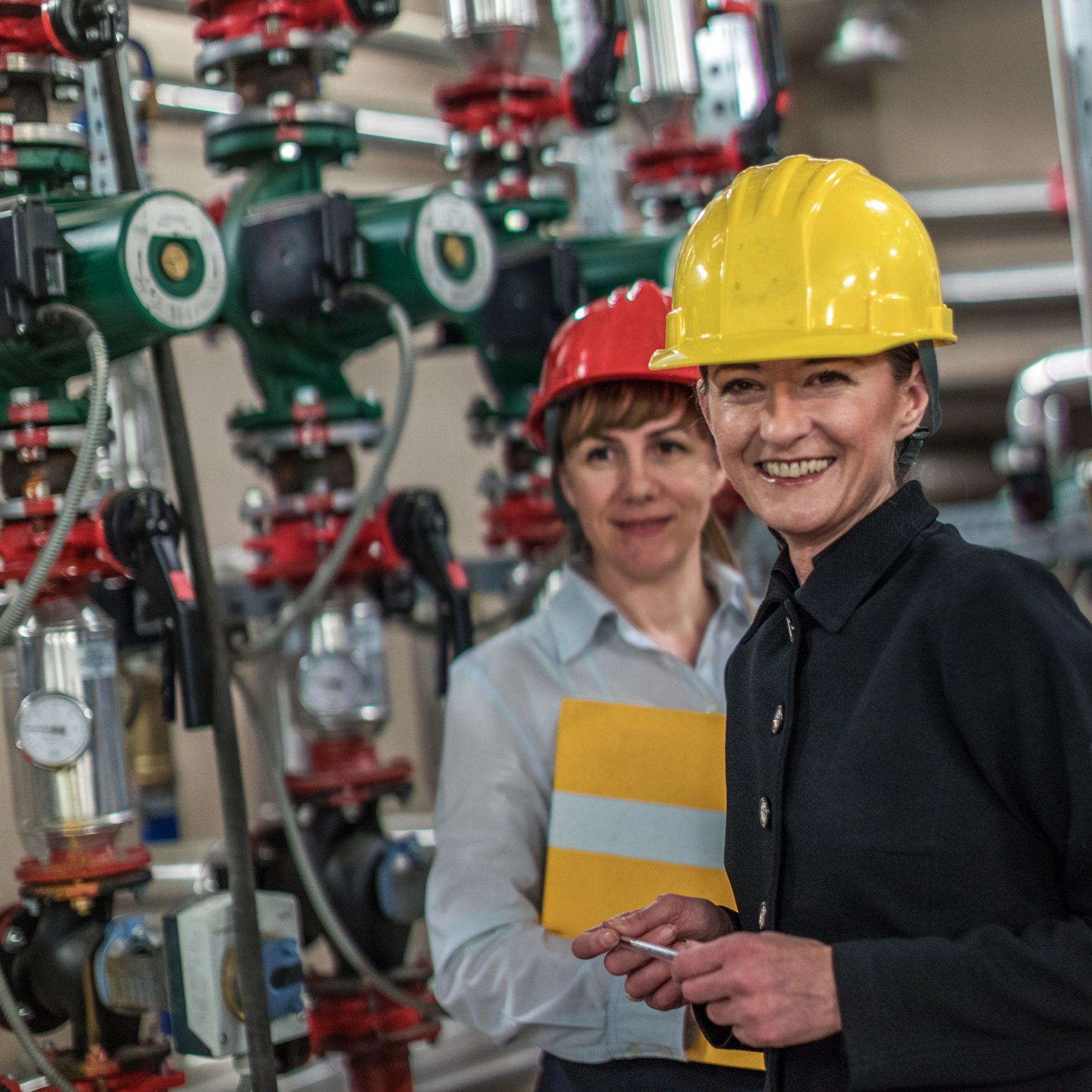 Two female engineers in hard hats inspecting industrial machinery.