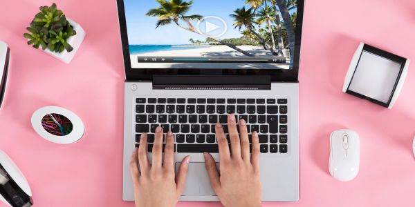 Person typing on laptop with tropical beach video on screen.