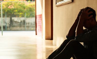 A person sitting on the floor holding their head in distress.