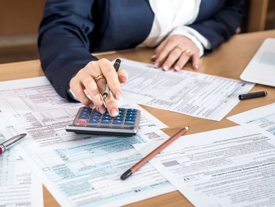 Person calculating taxes with a calculator and tax documents on a desk.