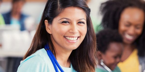 Smiling volunteer with stethoscope, helping a child and mother.