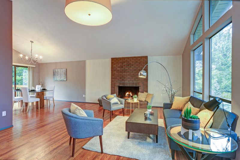 Lovely spacious open floor plan with vaulted ceiling and tan walls features living area with brick wall fireplace and polished hardwood floor.