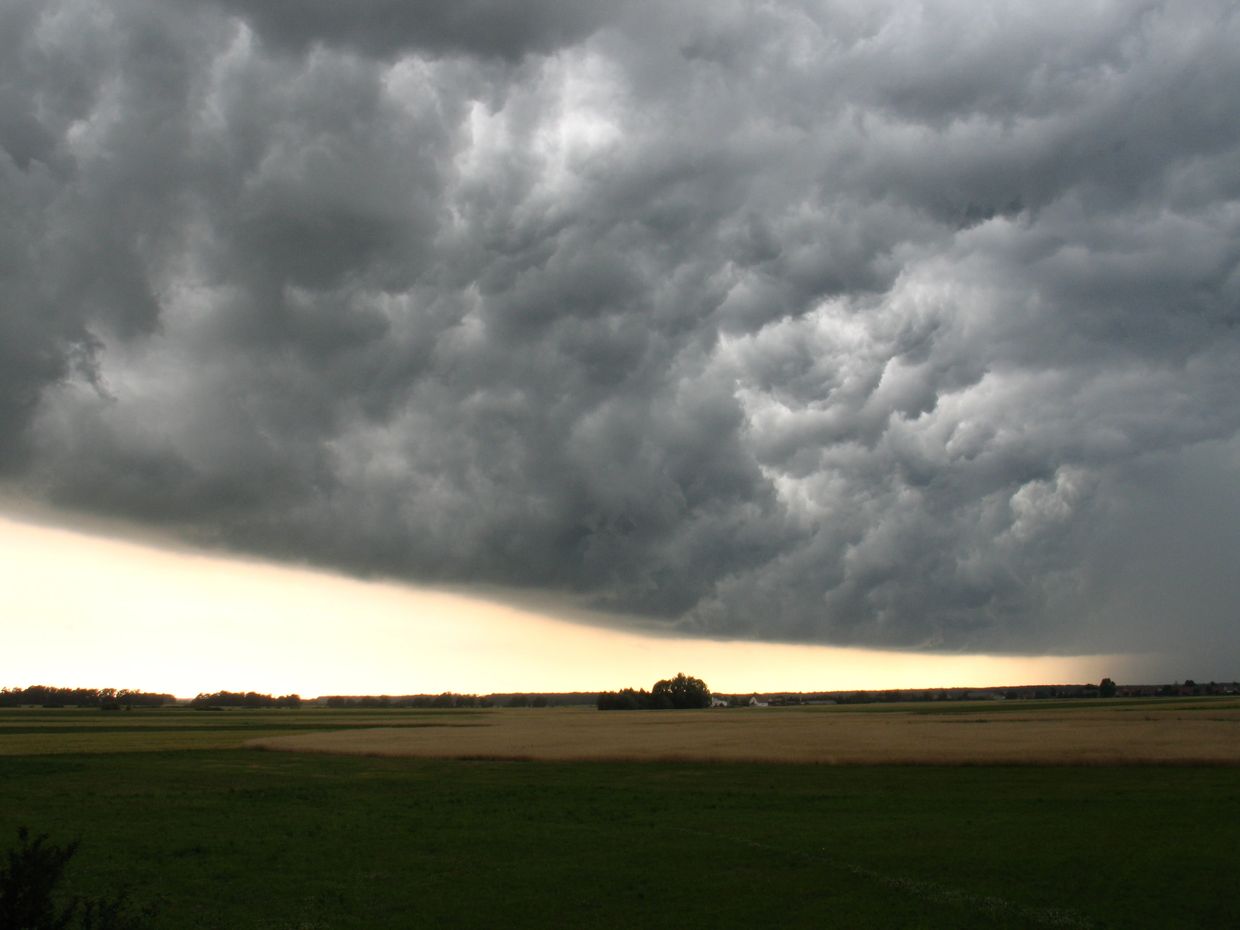 Dark storm clouds gather over a flat rural landscape.