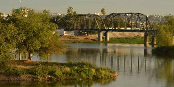 Puente metálico sobre un río rodeado de árboles.