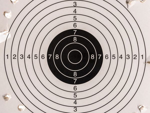 A paper shooting target with multiple bullet holes around the edges.