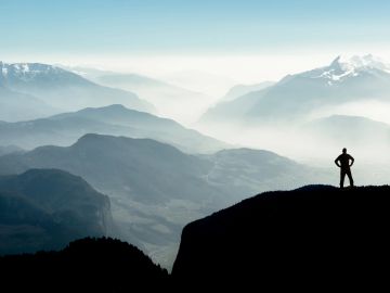 Person standing on cliff overlooking foggy mountains.