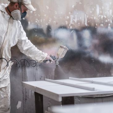 Worker spray painting a surface with protective gear in an industrial setting.