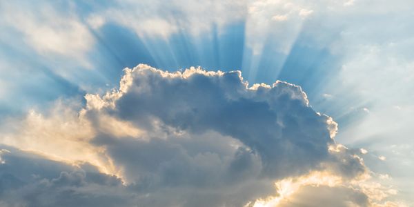 Sunlight rays burst through a large cloud in the sky.