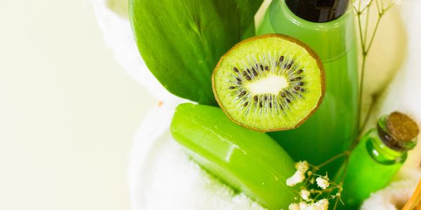 Green kiwi-themed spa products arranged with a white towel and flowers.